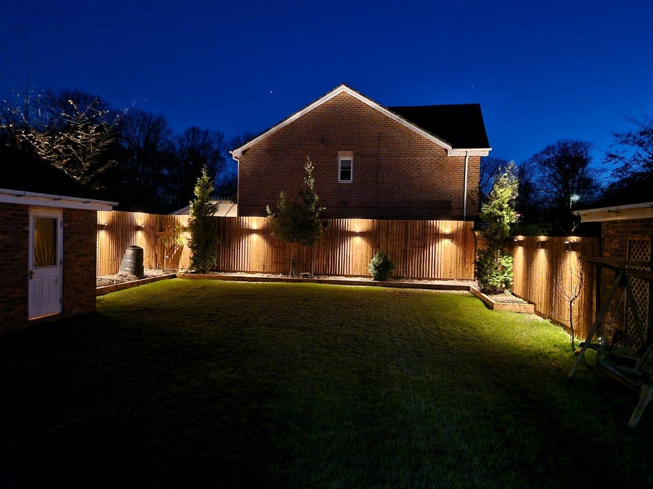 Garden lighting installed by Fishers Electrical Services in Chorley, warm wall lights on a timber fence